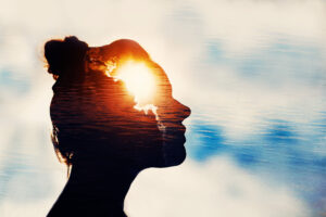 Double exposure: silhouette of a person’s profile overlaid with a sunset and calm ocean waves, creating a dreamy, contemplative scene.